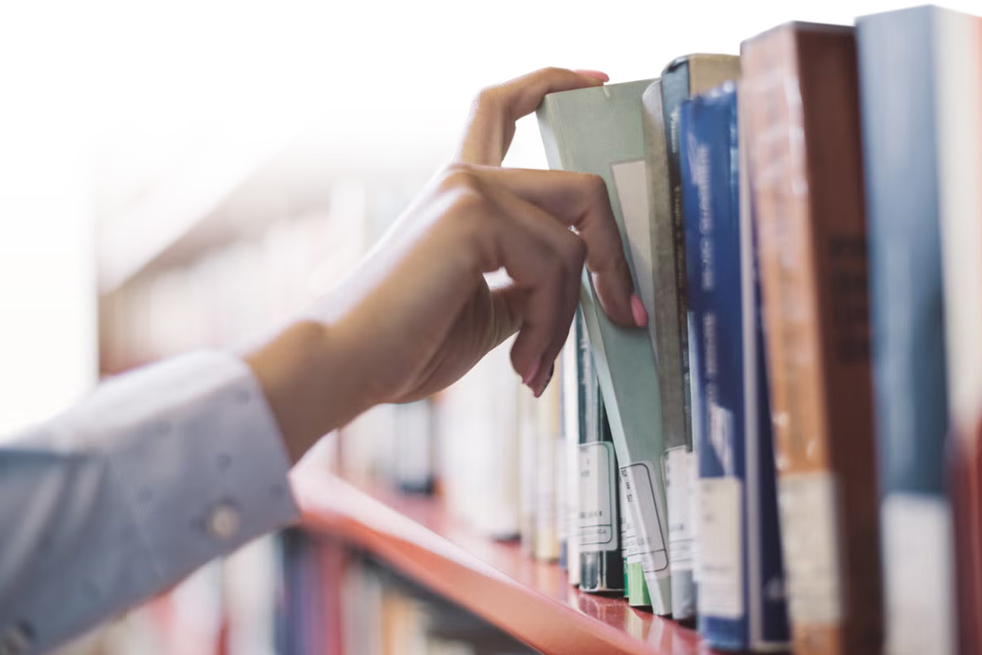 Pessoa pegando livro na estante de biblioteca